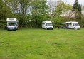 Campsite field with our three motorhomes parked at one end. The grass is uneven and slopes downwards a little.