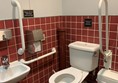 Overview of toilet showing sink, handrails, toilet, red cord and some floor space