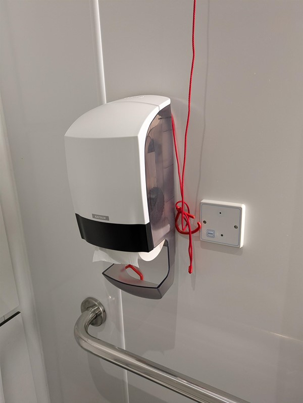 Image of red cord tied behind toilet roll dispenser