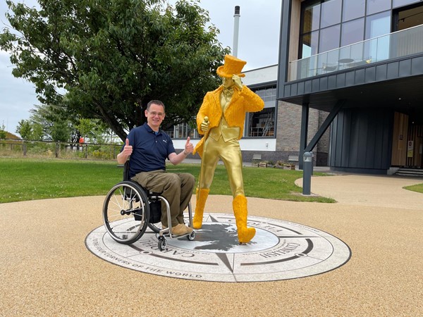 Paul sitting by the yellow jacketed String Man statue at the from of the main entrance to Clynelish Distillery