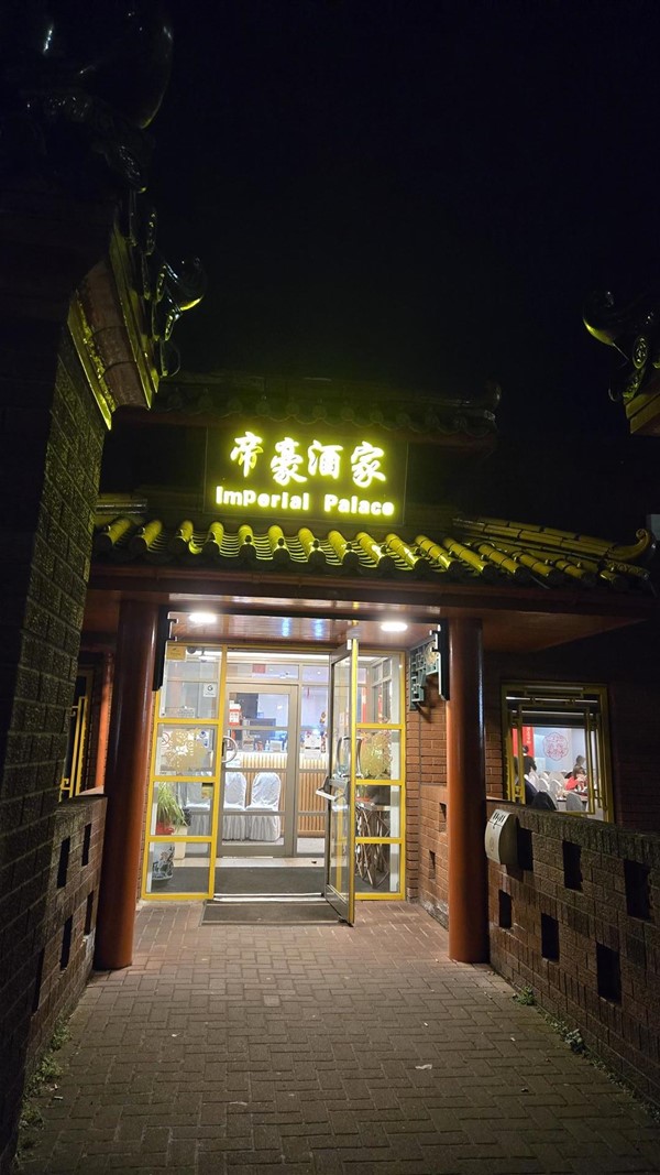 A wider shot of the restaurant's main entrance, showing the illuminated "Imperial Palace" sign above the door. The flat street leading up to the entrance is also visible.
