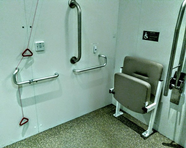 Extra large fitting room with alarm cord handles and folding seat for wheelchair users.