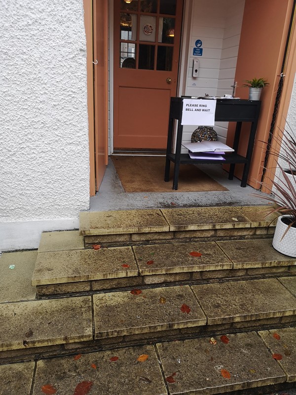 The entrance with 4 steps leading up to it. There is a sign asking you to ring the bell and hand sanitiser can be seen attached to the wall.