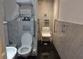 Bathroom from doorway, showing shower chair, toilet and half of the sink.