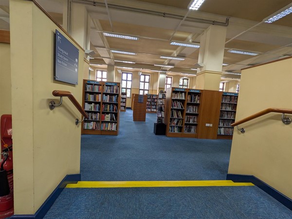 Image of the stairs from a raised section in the library, there are yellow markings at the stair edges and handrails on either side.