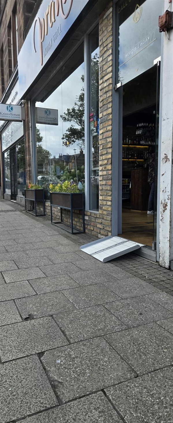 The entrance to Prahna Indian Grill. A portable metal ramp has been placed over a step at the doorway, and the glass entrance door is propped open.