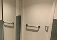 Image of the inside of the bathroom door. There is a handrail on the back of the door and it locks by lifting up the handle. There is a full-length mirror on the wall to the left of the door.