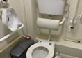 View of toilet from door showing handrails, toilet roll holder is open