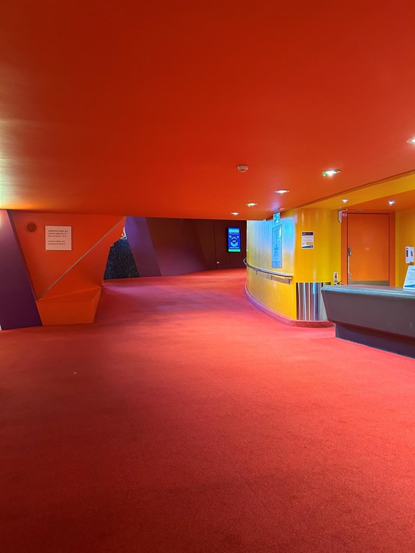 Image of a red carpeted hallway with a red wall and a blue sign