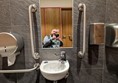 Image of a person taking a selfie in a mirror over a sink with grabrails