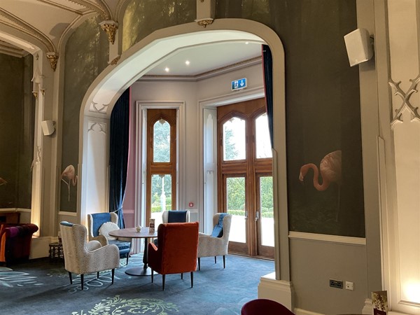 GARDEN ROOM. Directly opposite The Oak room, you will enter the nicely decorated “Garden Room” this is a very interesting quiet place to enjoy reading your favourite book of the day, while relaxing in one of its softly cushioned sofas or a high backed chair. Each wall is lined with Flamingoes either in wooden frames, or as a wallpaper wall. It is a pleasant escape, worth going to see. The soft lightening hints of gold, lovely chandeliers highlight its historical period, and the carpet has been selected well to bring to life the whole room.
