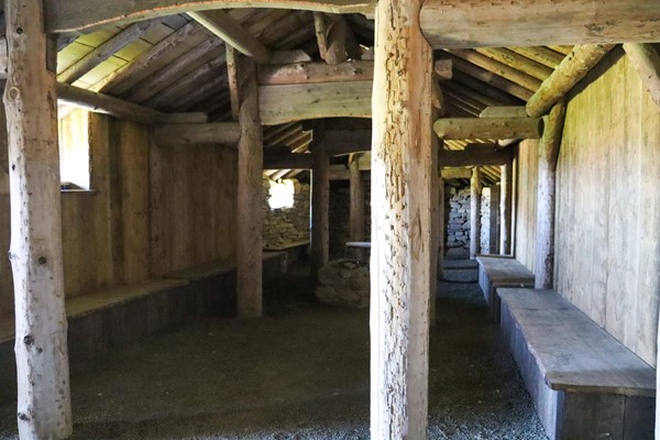 Inside the longhouse with wooden pillars and benches around the edge.