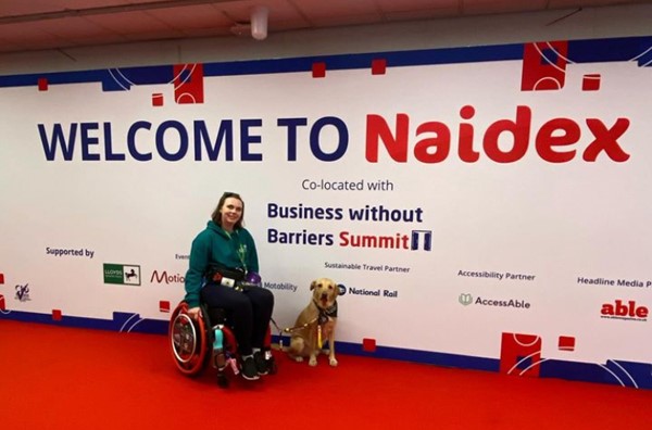 Image of a person and dog in front of a Naidex sign