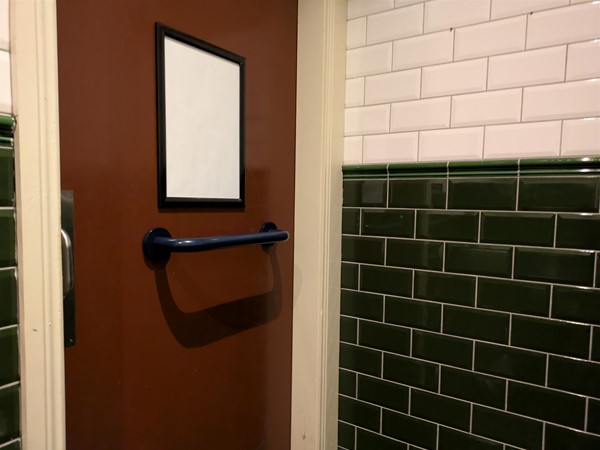 Image of door to the accessible toilet with a blue grabrail