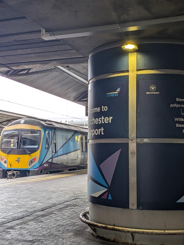 Image of a train, with a pillar that reads Welcome to Manchester Airport