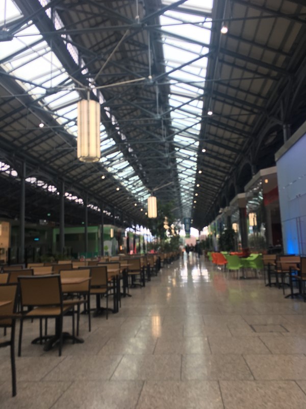 Walkway to gift shop and ticket booth. Tables and chairs are in the middle and cafes and small shops on either side.