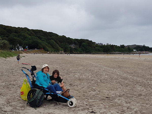Using the beach wheelchair on Marble Hill Strand with dunes and wooded cliffs behind