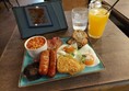 The all day breakfast on the cafe table: sausages, bacon, hash browns, two free range eggs, a potrabello mushroom, beans and sourdough toast. Fresh squeezed orange juice and a glass of water. Claire's kindle is propped up behind the plate.