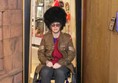 Lady in wheelchair wearing guard's jacket and hat.