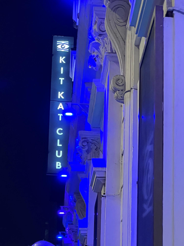 Illuminated sign on side of building saying Kit Kat Club.