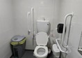 Accessible bathroom with grab rails on either side of the toilet and a sink positioned at a wheelchair-friendly height. A bin is placed close to the toilet, which may make transfers difficult for some users.
