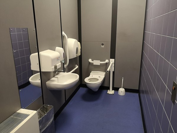 Shows the inside of the Male Accessible Toilet - confirming raised toilet, grab rails, wall arm and plenty of room to move around