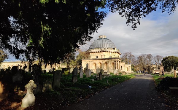 A view of the domed chapel in sunshine, framed by shaded trees in the foreground.