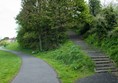 View of path in Redhall Park. On the right hand side there is a steep incline and steps between trees and bushes.