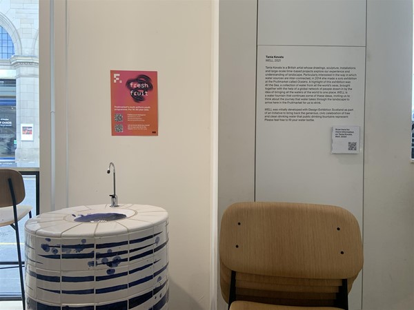 image of a blue and white tiled water fountain next to a sign on the wall and a stack of chairs