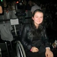 Photo of me in my manual wheelchair at a concert holding my mobile phone