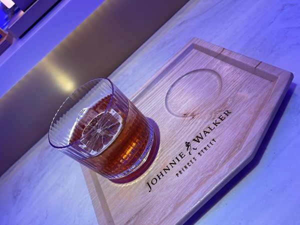 Trying a drink in the bar. A photo of the first drink sitting on a wooden platter engraved with the Johnnie Walker  "Striding Man" logo.